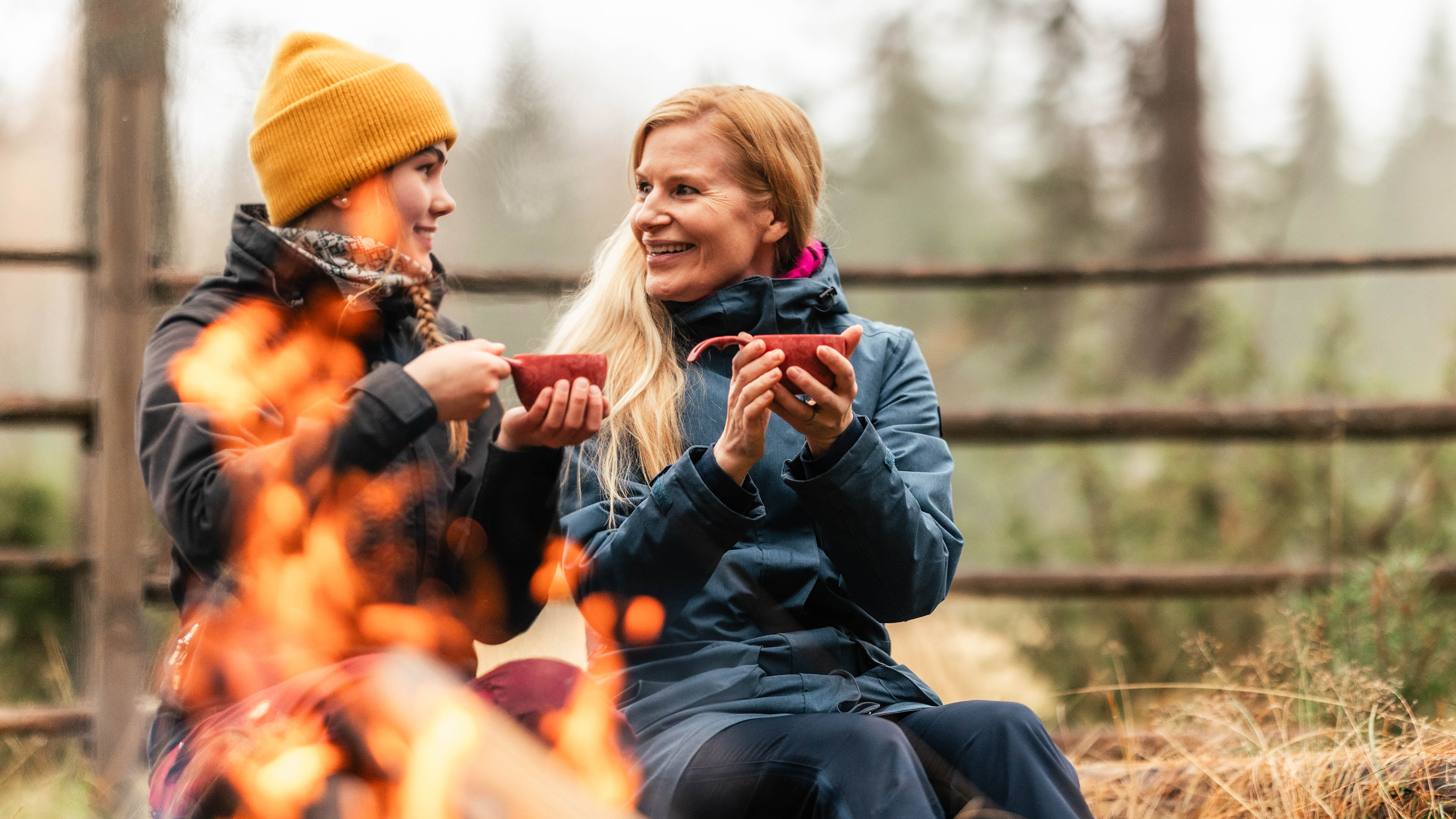 Two women enjoying coffee by fire in Taava Reindeer Farm, Rovaniemi.