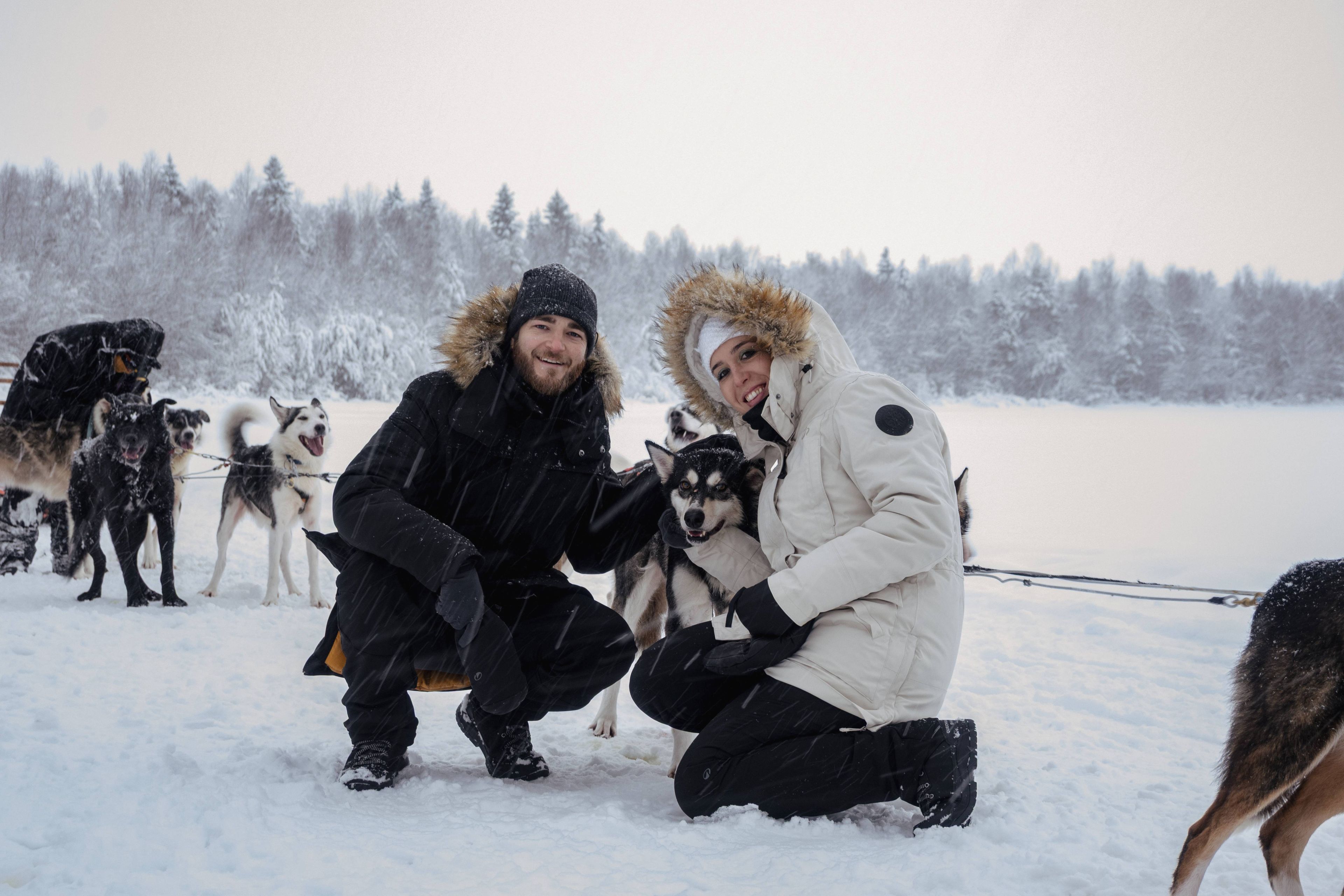 Two people posing with a husky in a snowy landscape.