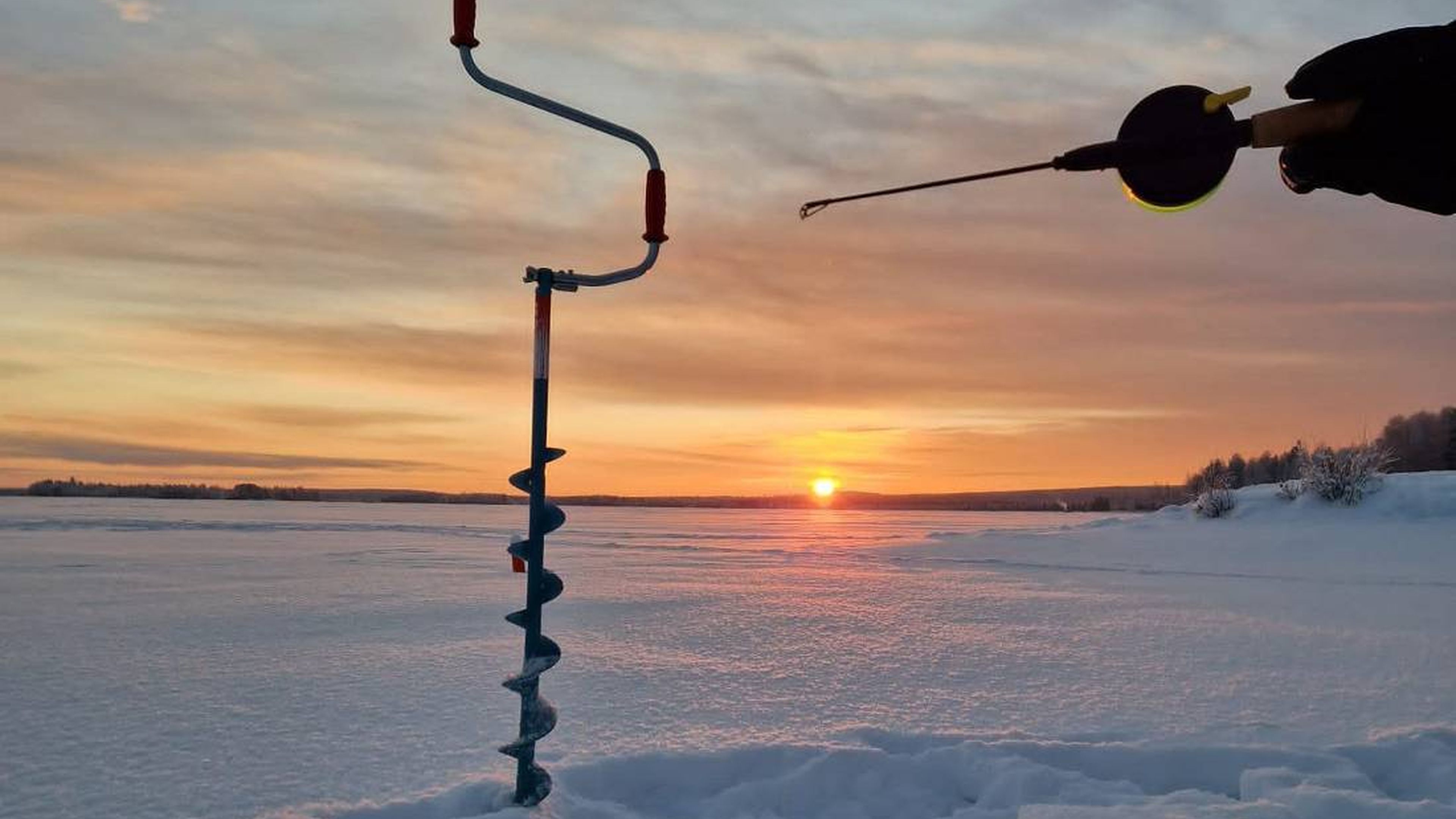 Ice fishing with a colourful sunset at the background.