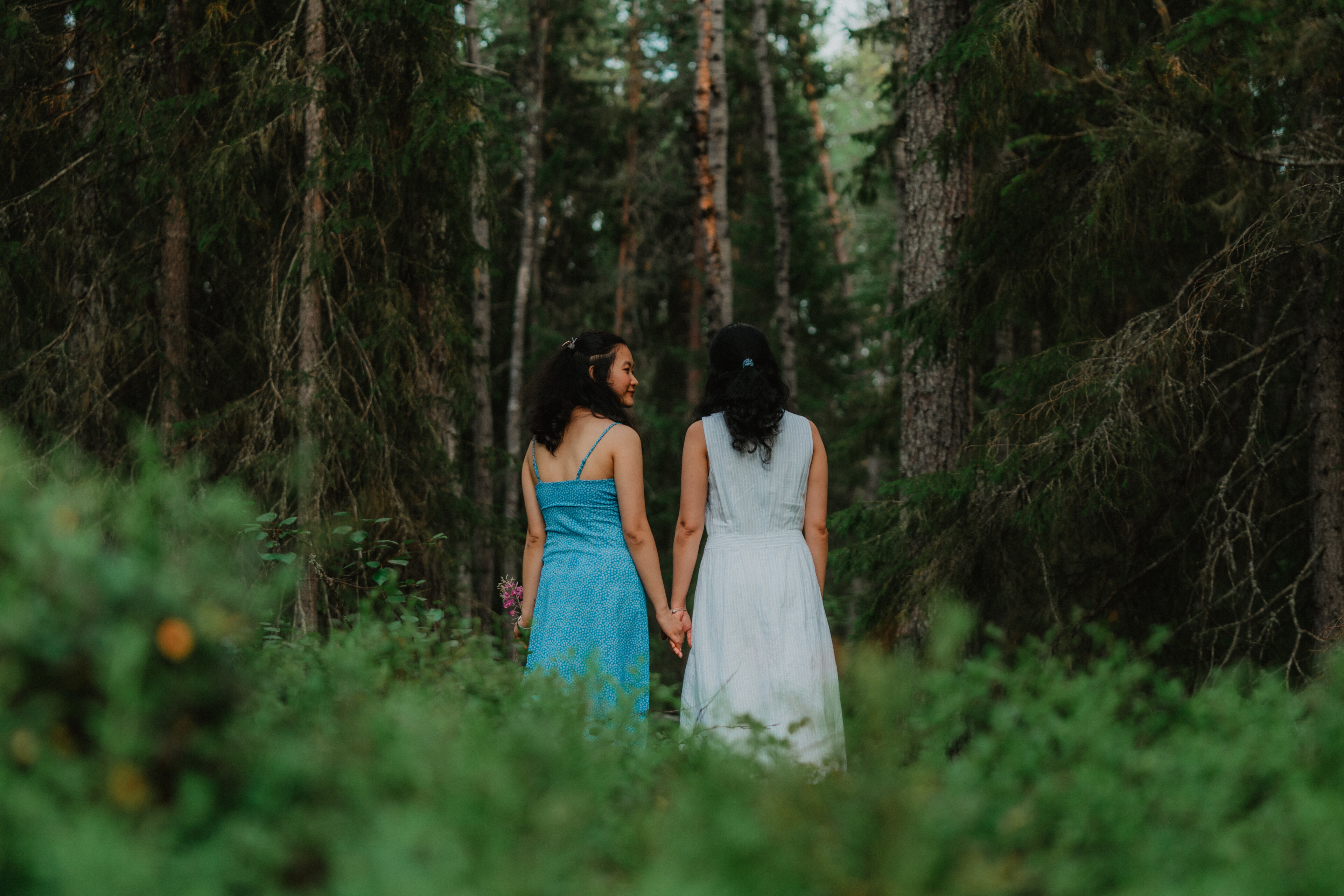 Two women walking a nature trail and holding hands in forest during summer in Rovaniemi, Lapland, Finland.