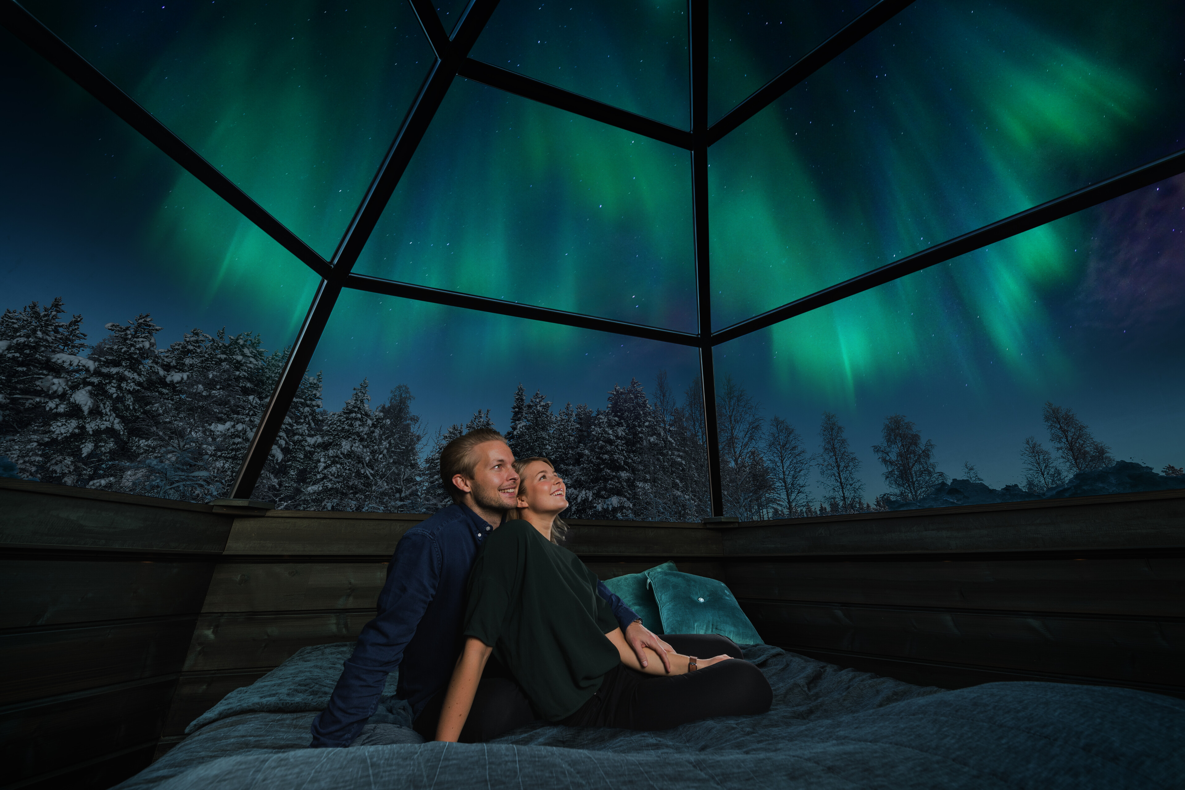 Couple watching from a glass igloo as Northern Lights are dancing in the sky in Rovaniemi, Lapland, Finland.
