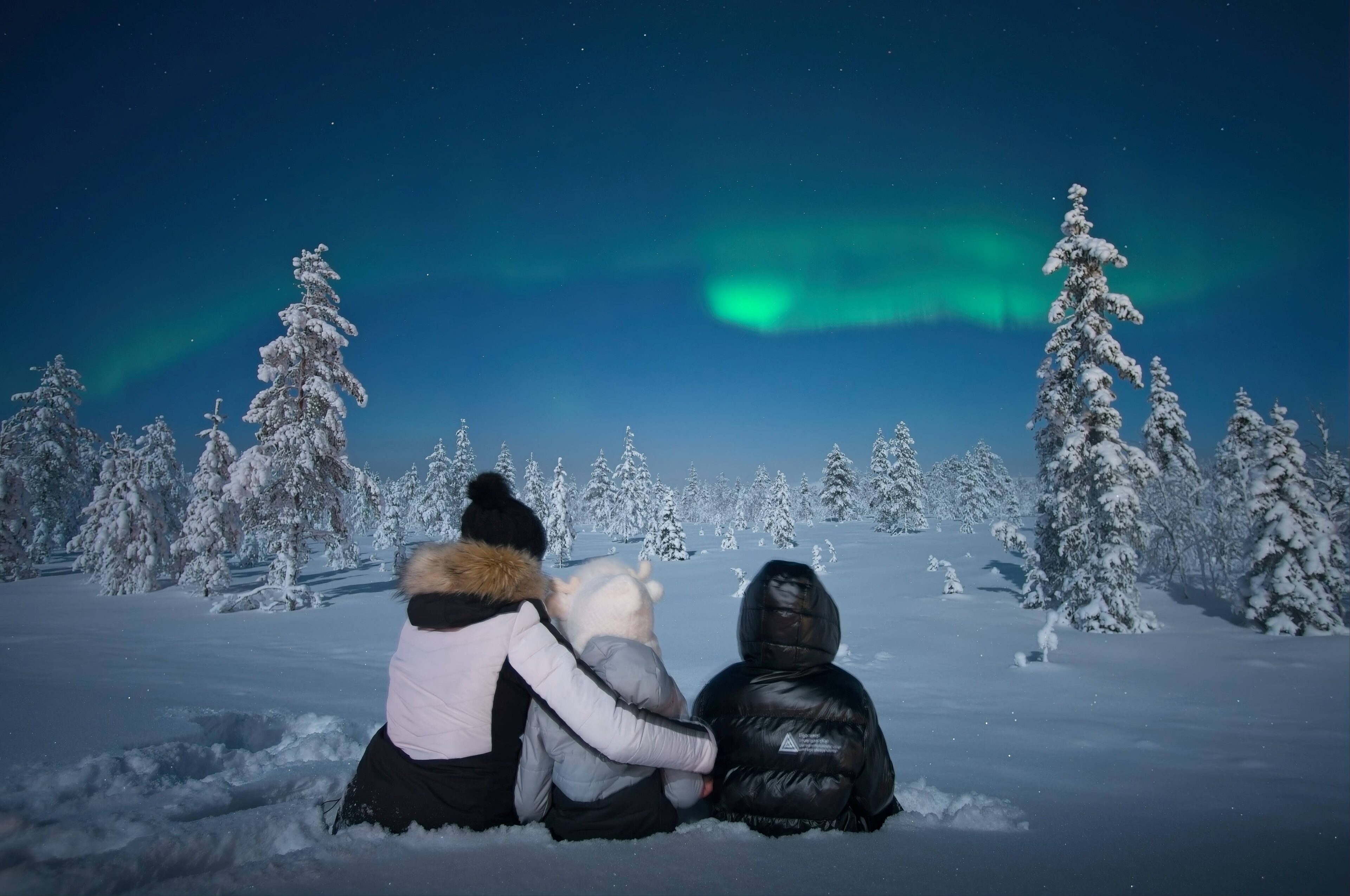 Family watching northern lights in Rovaniemi sitting in the snow.