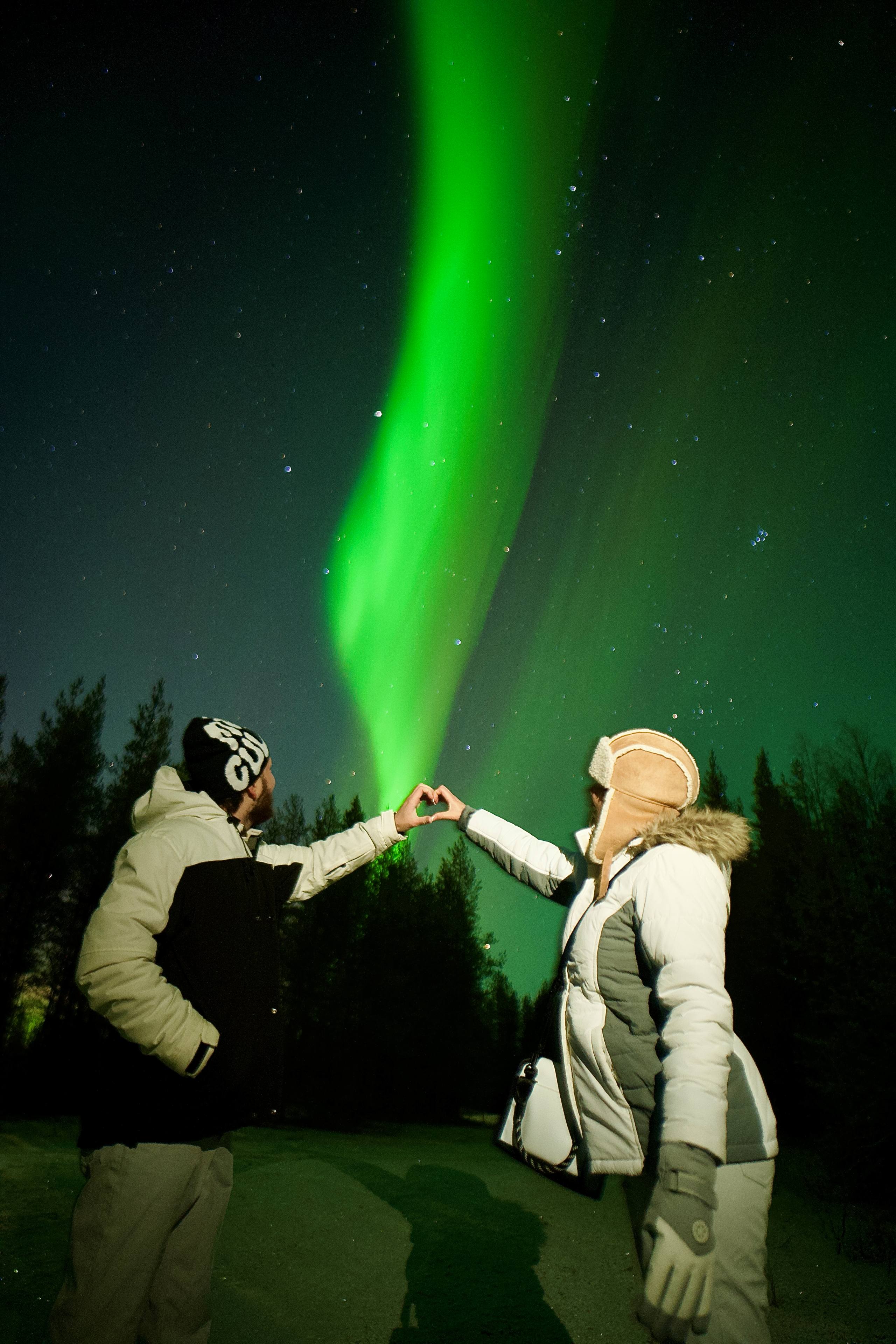 Couple forming heart with their hands under auroras, Authentic Experiences, Rovaniemi, Lapland, Finland
