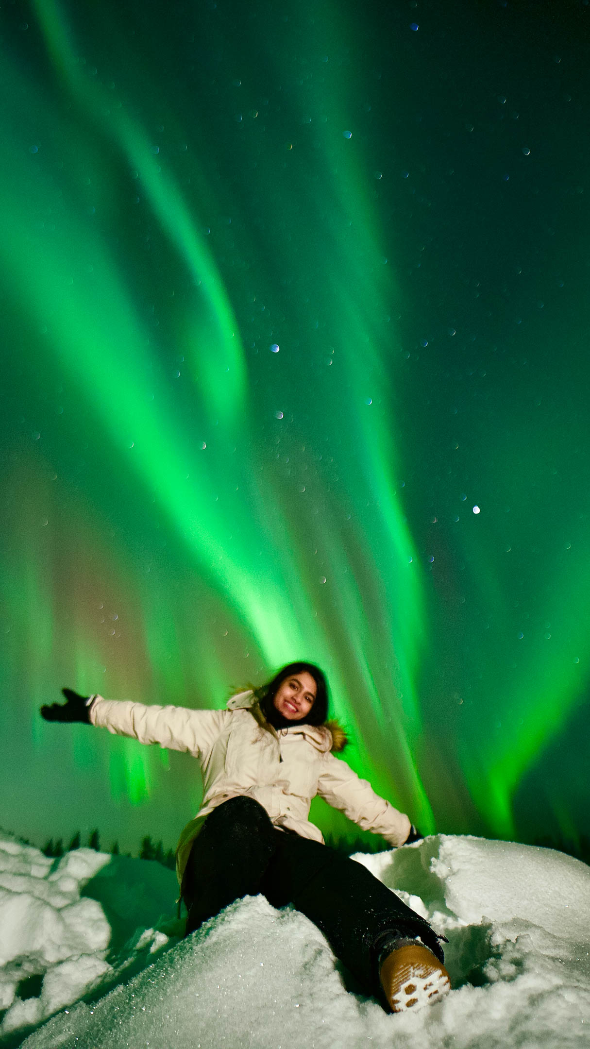 Person enjoying northern lights display on the top of pile of snow, Authentic Experiences, Rovaniemi, Lapland, Finland
