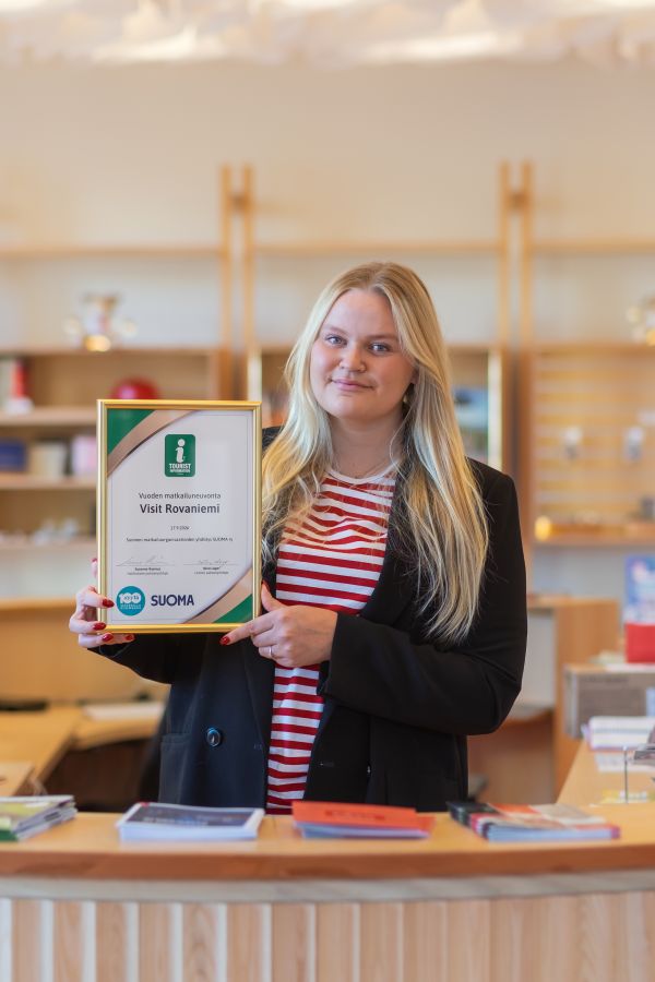 Rovaniemen matkailuneuvonnan työntekijä pitää Vuoden Matkailuneuvonta kylttiä