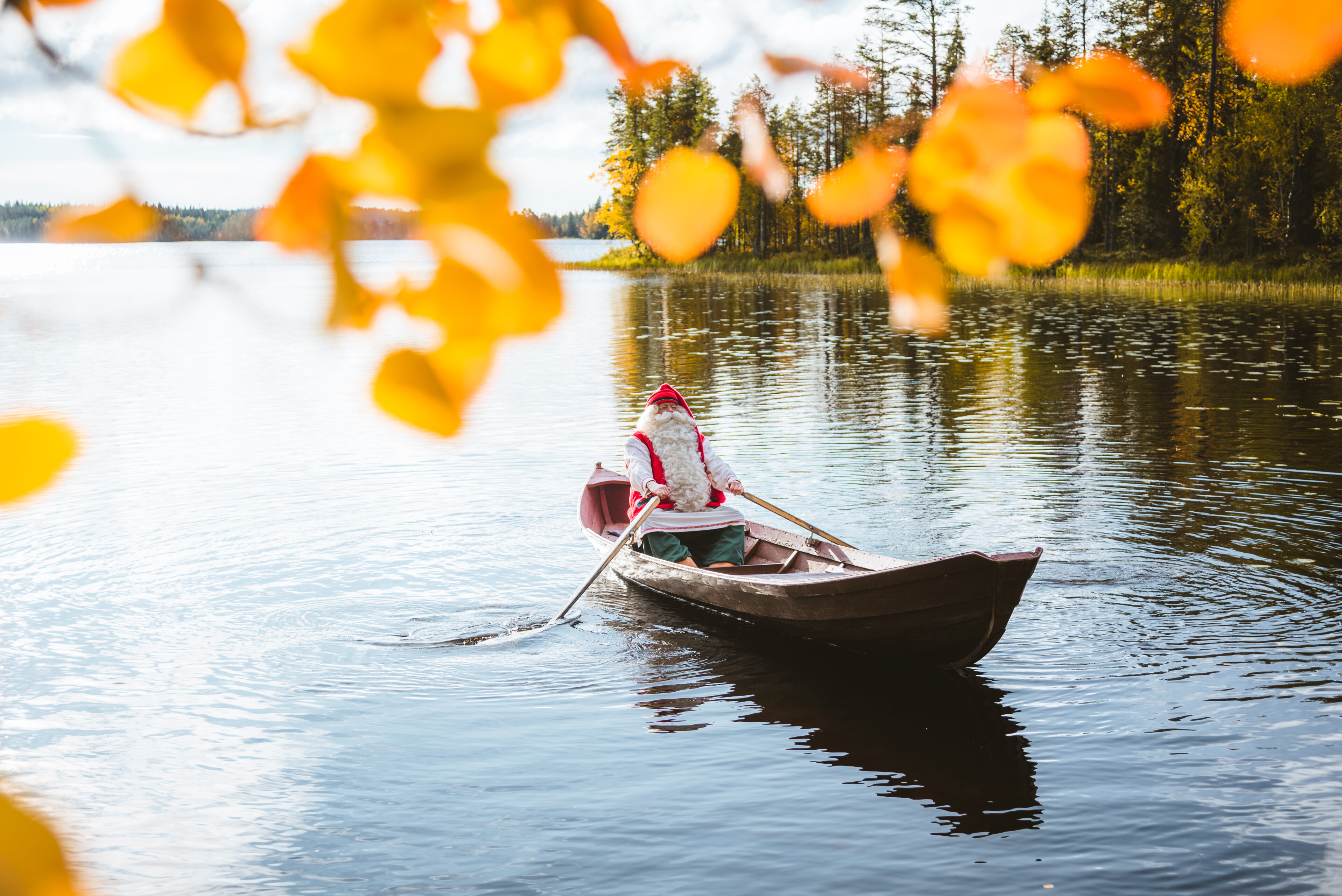 Joulupukki soutamassa järvellä syksyllä ruskan väreissä Rovaniemellä, Lapissa.