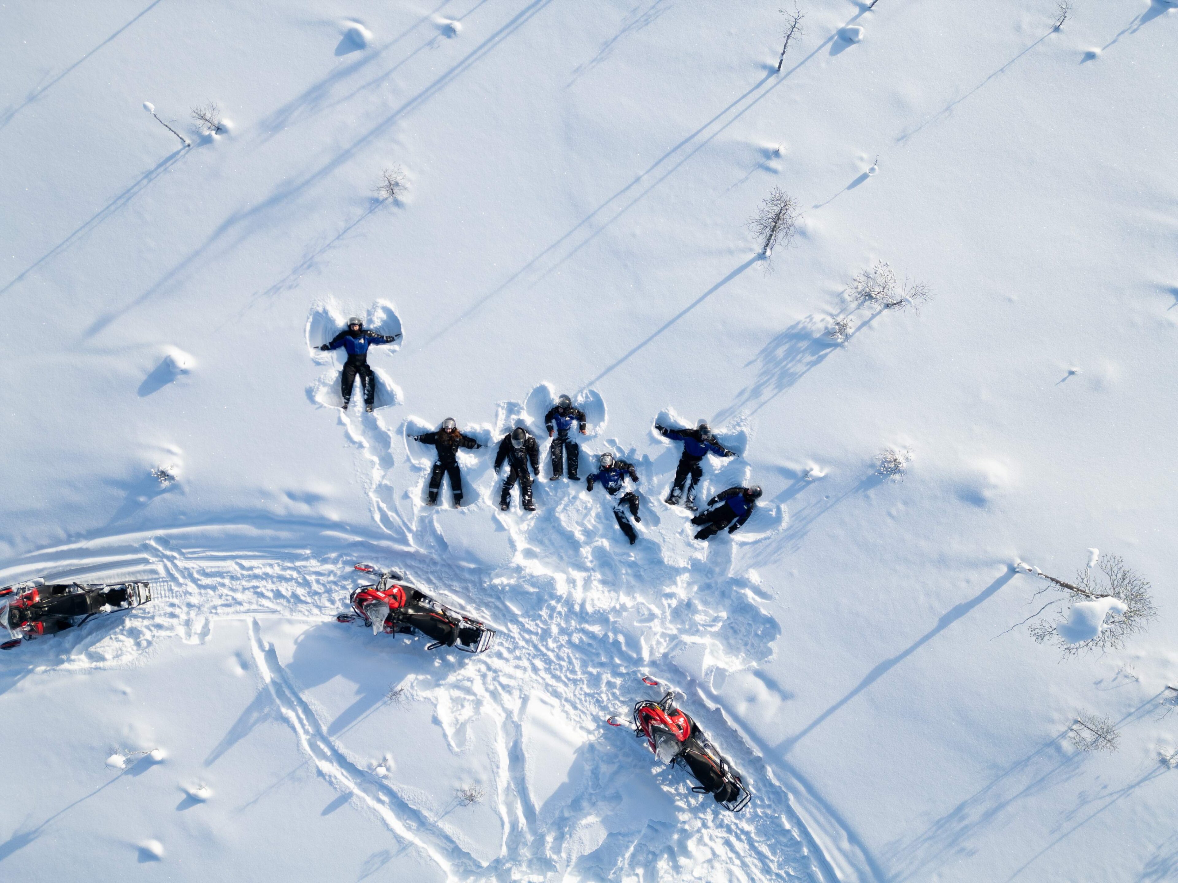 People making snow angels in snow next to snowmobile trail in Jauri Resort, Kemijarvi, Lapland, Finland