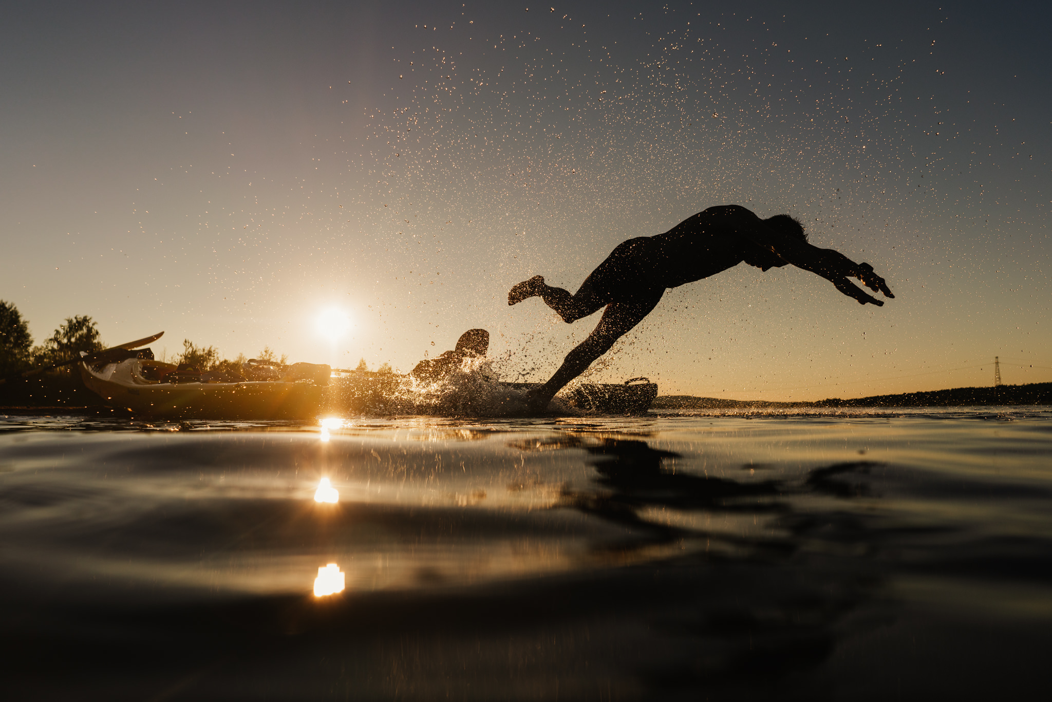 A person jumping in to water swimming during sunset in summer in Rovaniemi, Lapland, Finland.