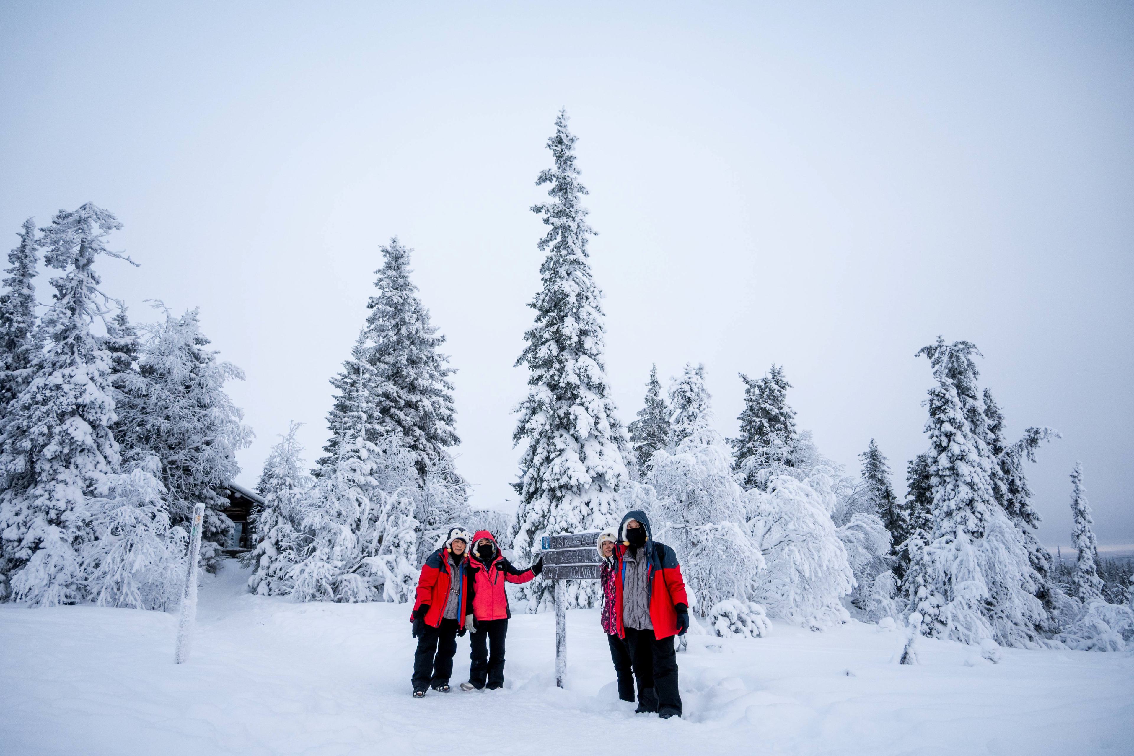 People standing in snowy forest in front of a sign.