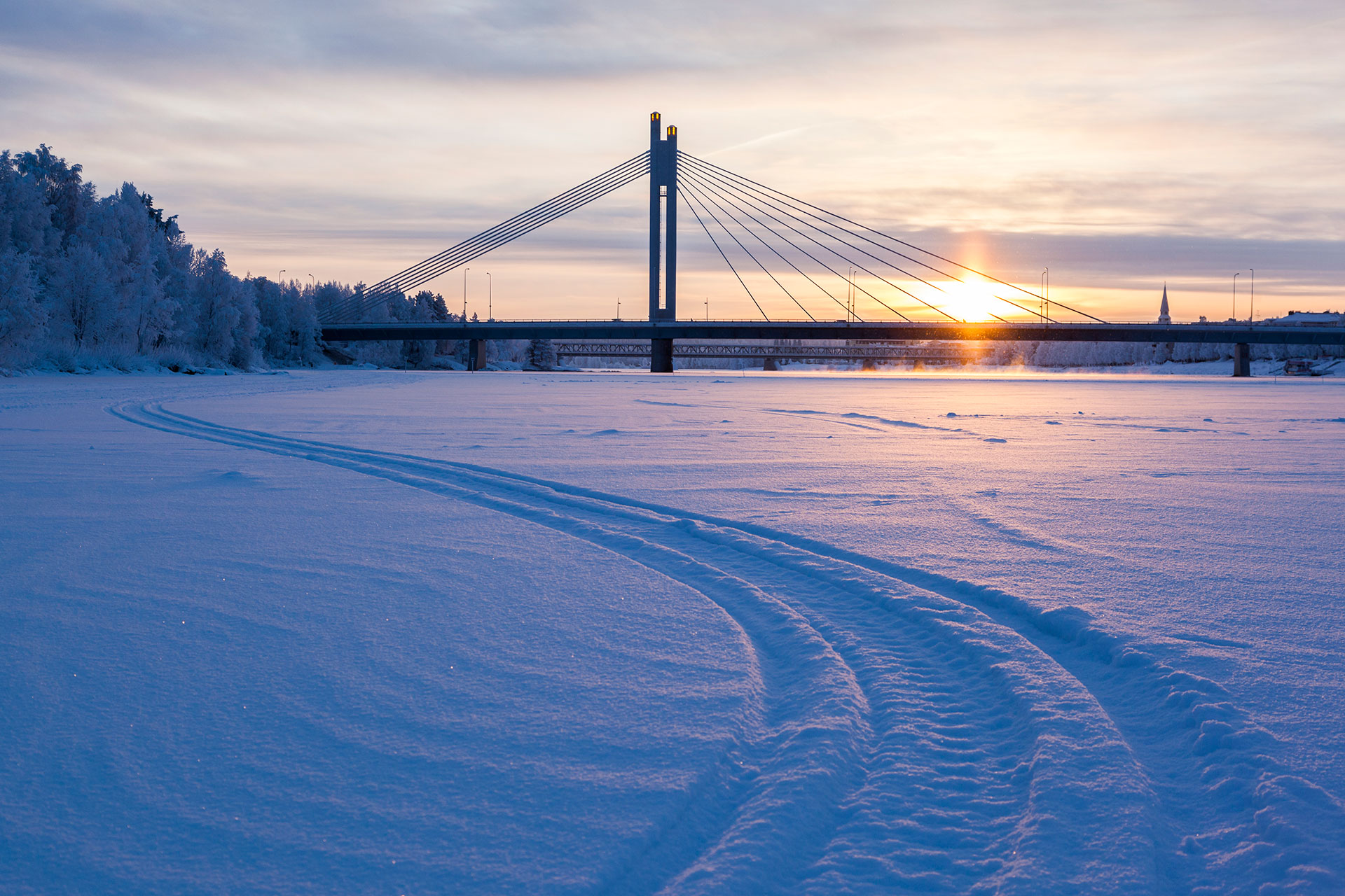 Snowmobile tracks on the river ice with Jatkankynttila bridge in the background, close to central Rovaniemi, Lapland, Finland